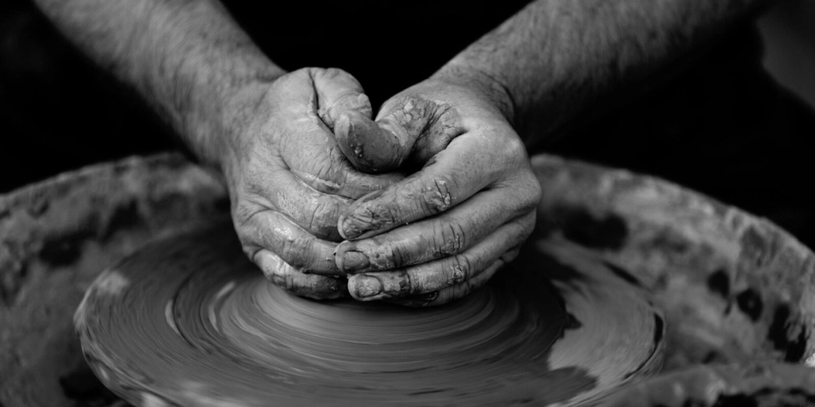 A potter's hands shaping wet clay on a spinning wheel.