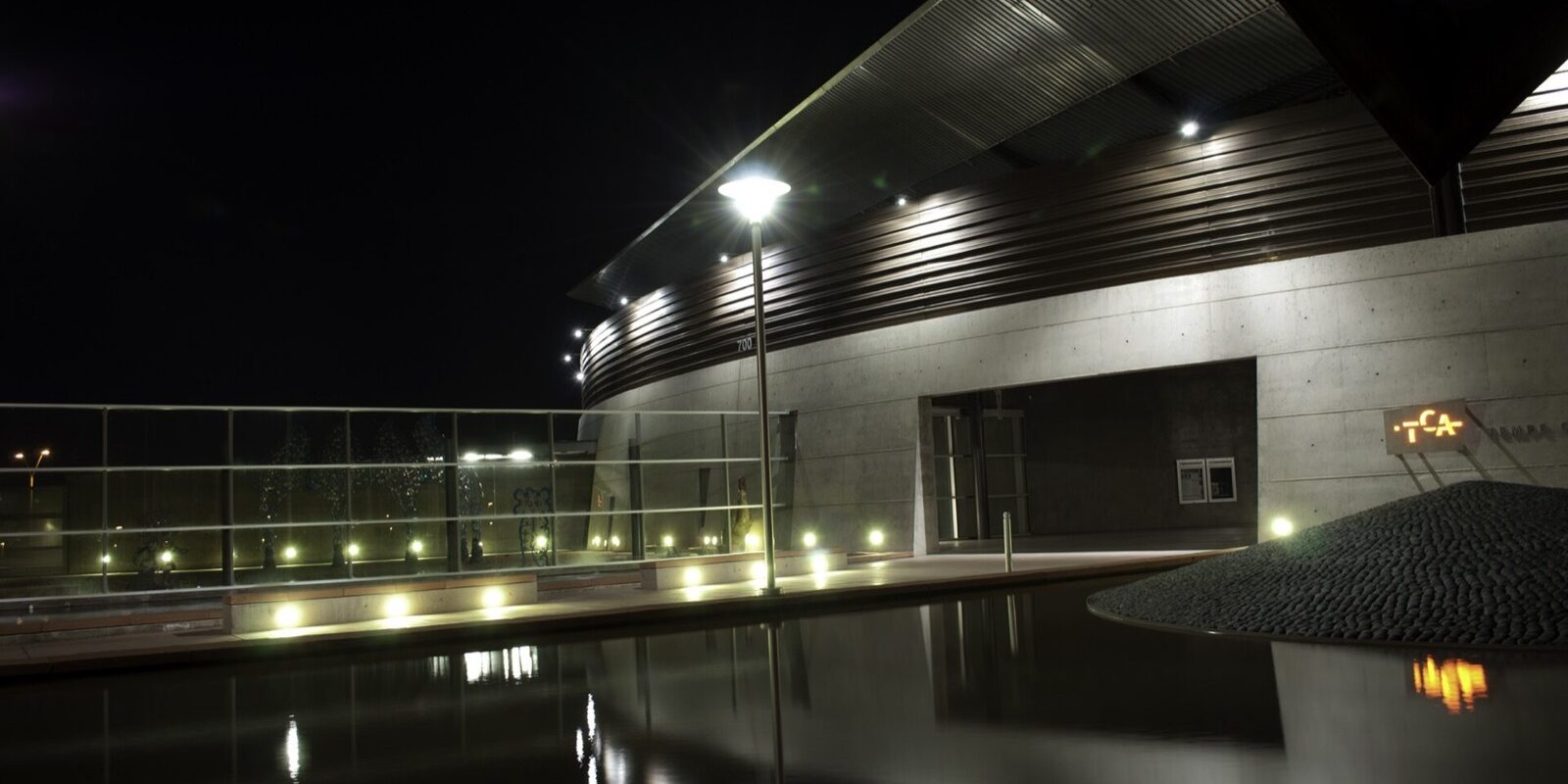 Tempe Center for the Arts at night, its angular metal roofline and lit lobby mirrored in the reflecting pool.