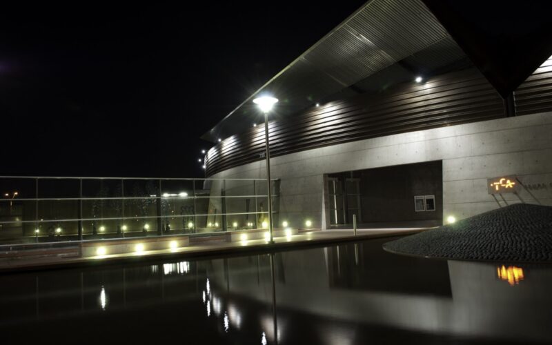 Tempe Center for the Arts at night, its angular metal roofline and lit lobby mirrored in the reflecting pool.